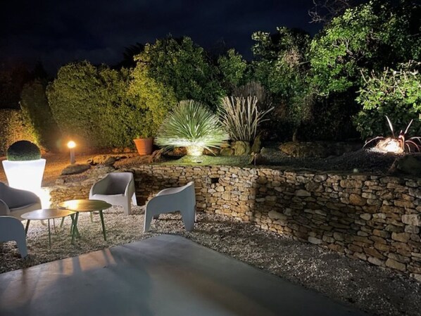 Un patio al aire libre con muros de piedra, un espacio de descanso y diversas plantas.