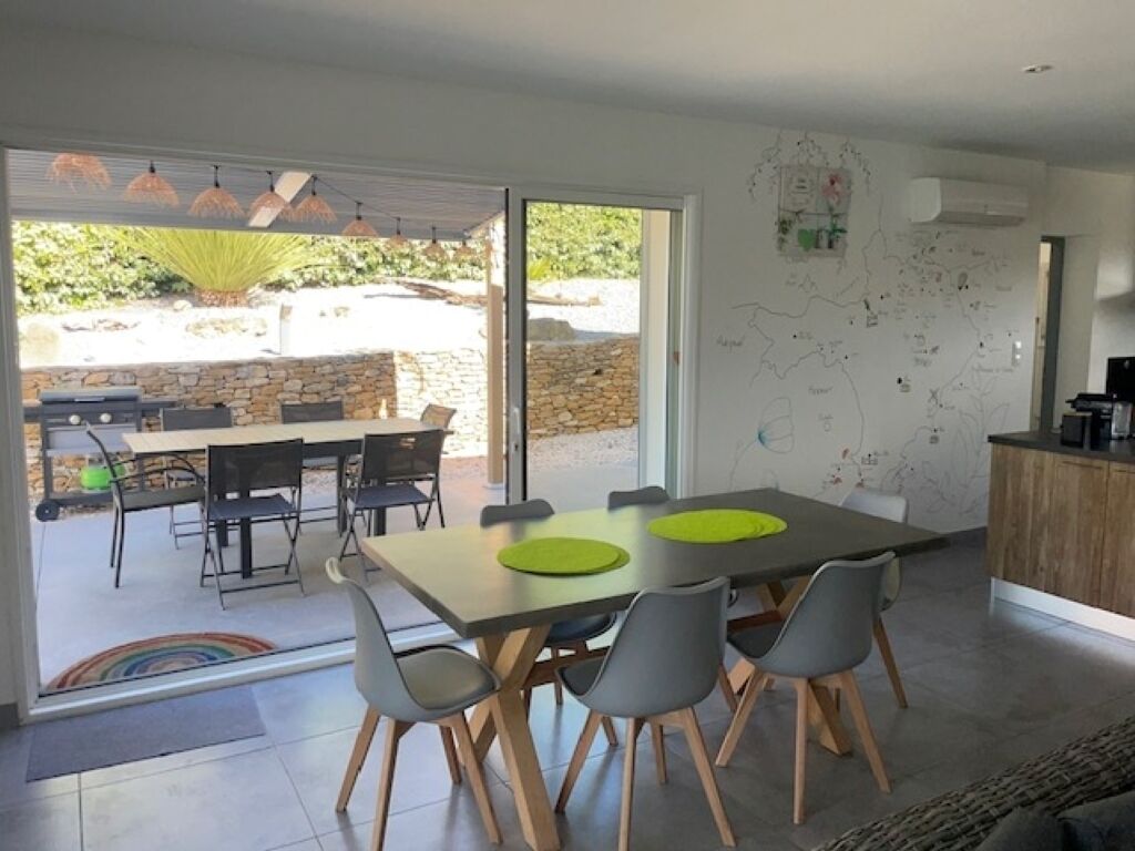 A modern dining area with a large table, chairs, and a kitchen area visible through an open door.