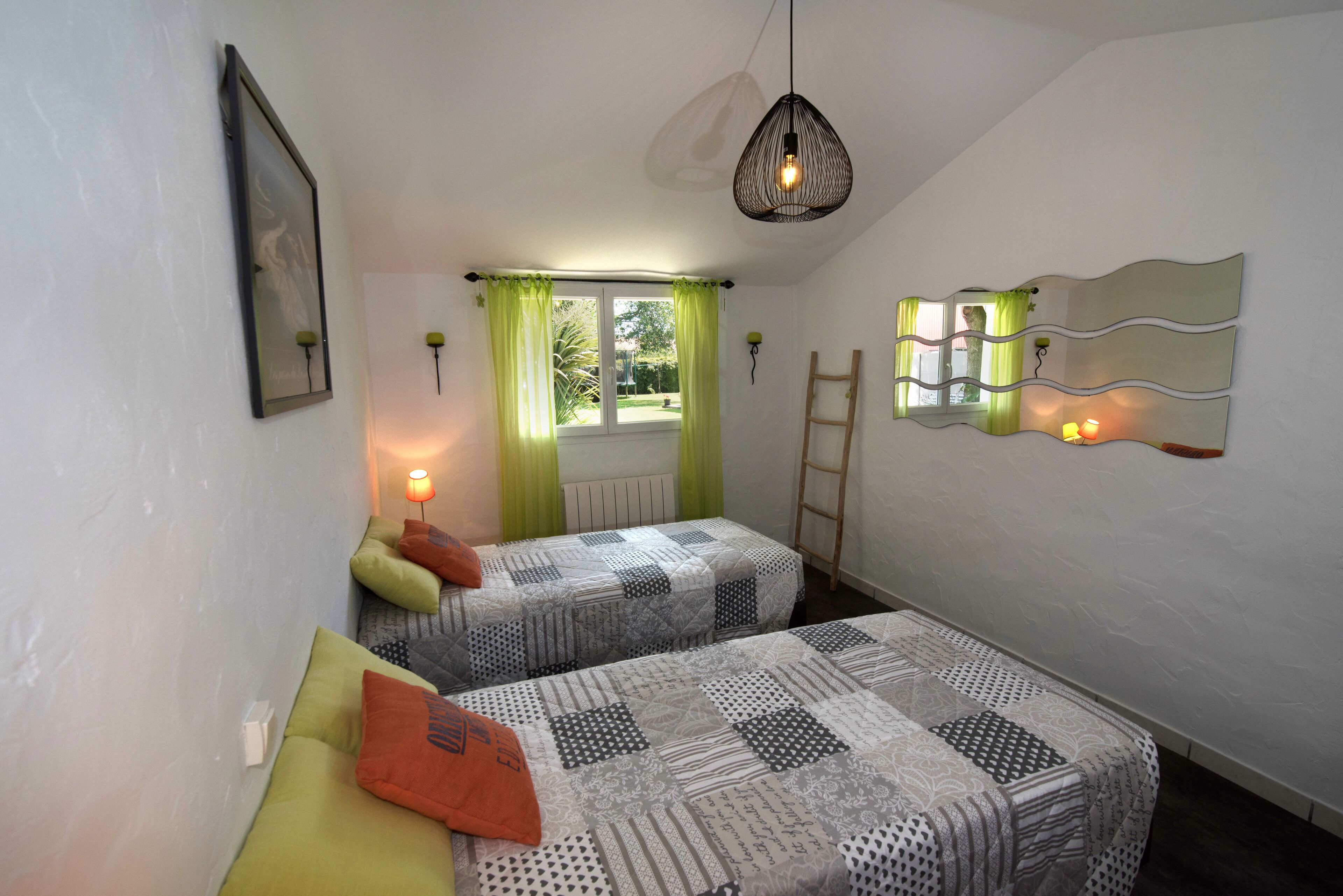 Een slaapkamer met twee bedden, een raam met gordijnen, een hanglamp en een spiegel aan de muur.