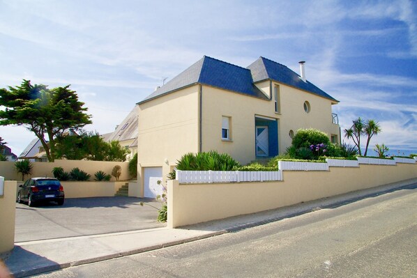 A two-story house with a blue roof, a front garage, and a white fence with greenery.