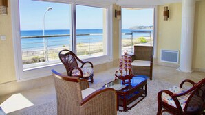 A spacious living area with large windows overlooking a beach, wicker furniture, and a decorative ship model.
