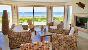 A room with wicker furniture, a glass coffee table, and large windows offering a view of the beach.