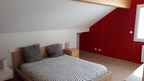 A bedroom with a bed, two bedside tables, and a red wall.