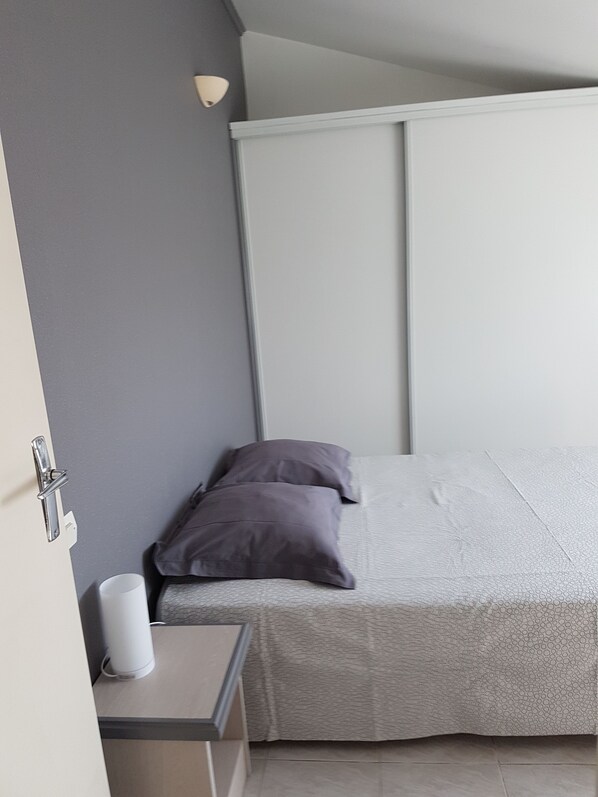 A small, modern bedroom with a bed, two pillows, a bedside table with a lamp, and a cup. - House located in the countryside (Mollégès)