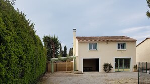 A two-story house with a gravel driveway, a covered patio, and a fenced yard. - House located in the countryside (Mollégès)