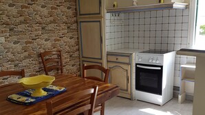 A kitchen with a stone wall, a tiled backsplash, a stove, and a dining table with chairs. - House located in the countryside (Mollégès)