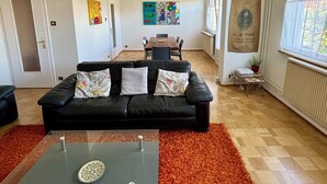 A modern living room with a black leather sofa, a glass coffee table, and a vibrant painting on the wall. - 3 Storks, House 9 acres, Alsace Centre (Châtenois)