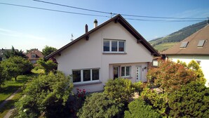 A two-story house with a sloped roof, multiple windows, and a garden with various plants and flowers. - 3 Storks, House 9 acres, Alsace Centre (Châtenois)