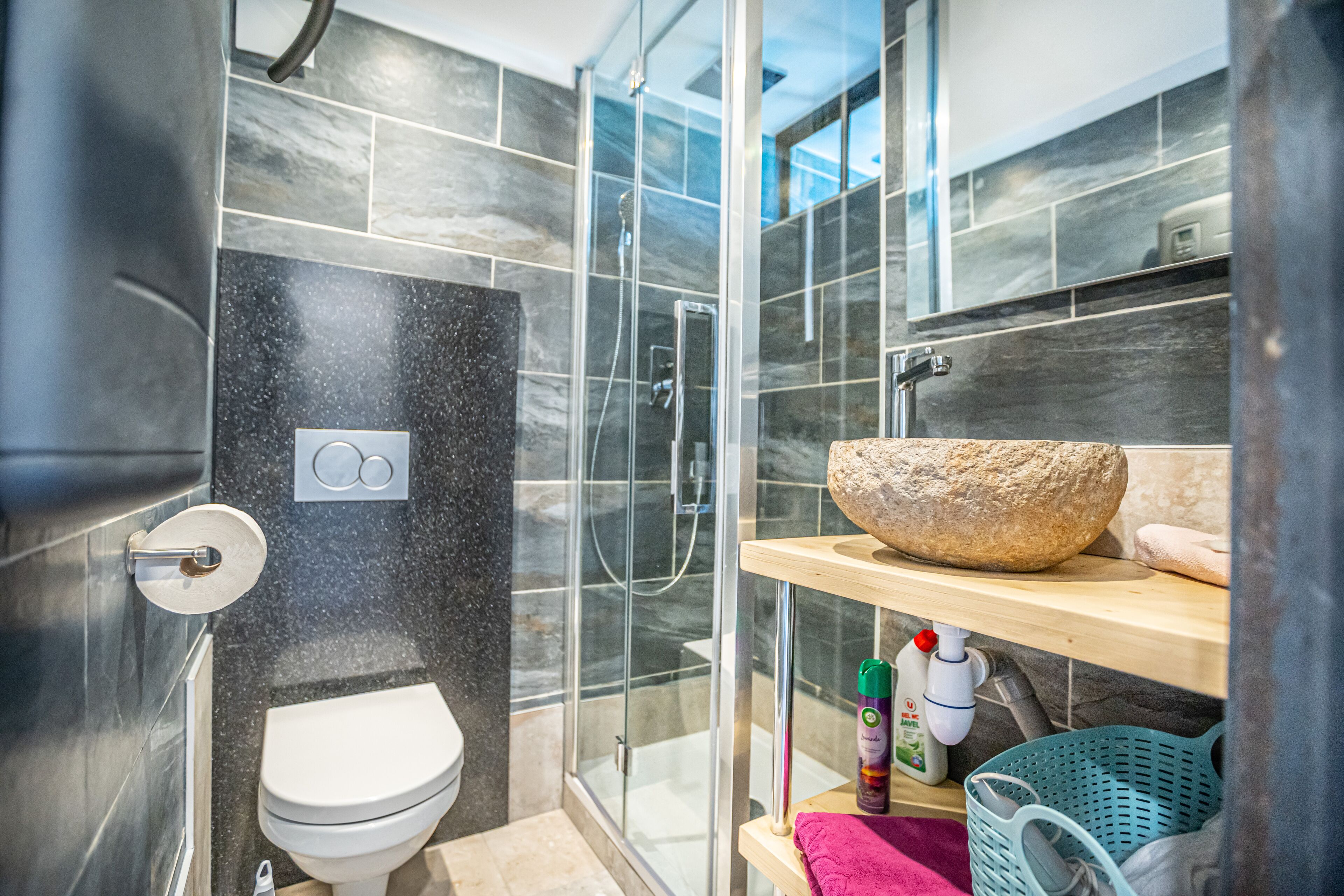 A modern bathroom with a glass-enclosed shower, a white toilet, and a wooden vanity with a large bowl sink.