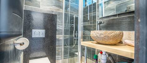 A modern bathroom with a glass-enclosed shower, a white toilet, and a wooden vanity with a large bowl sink.