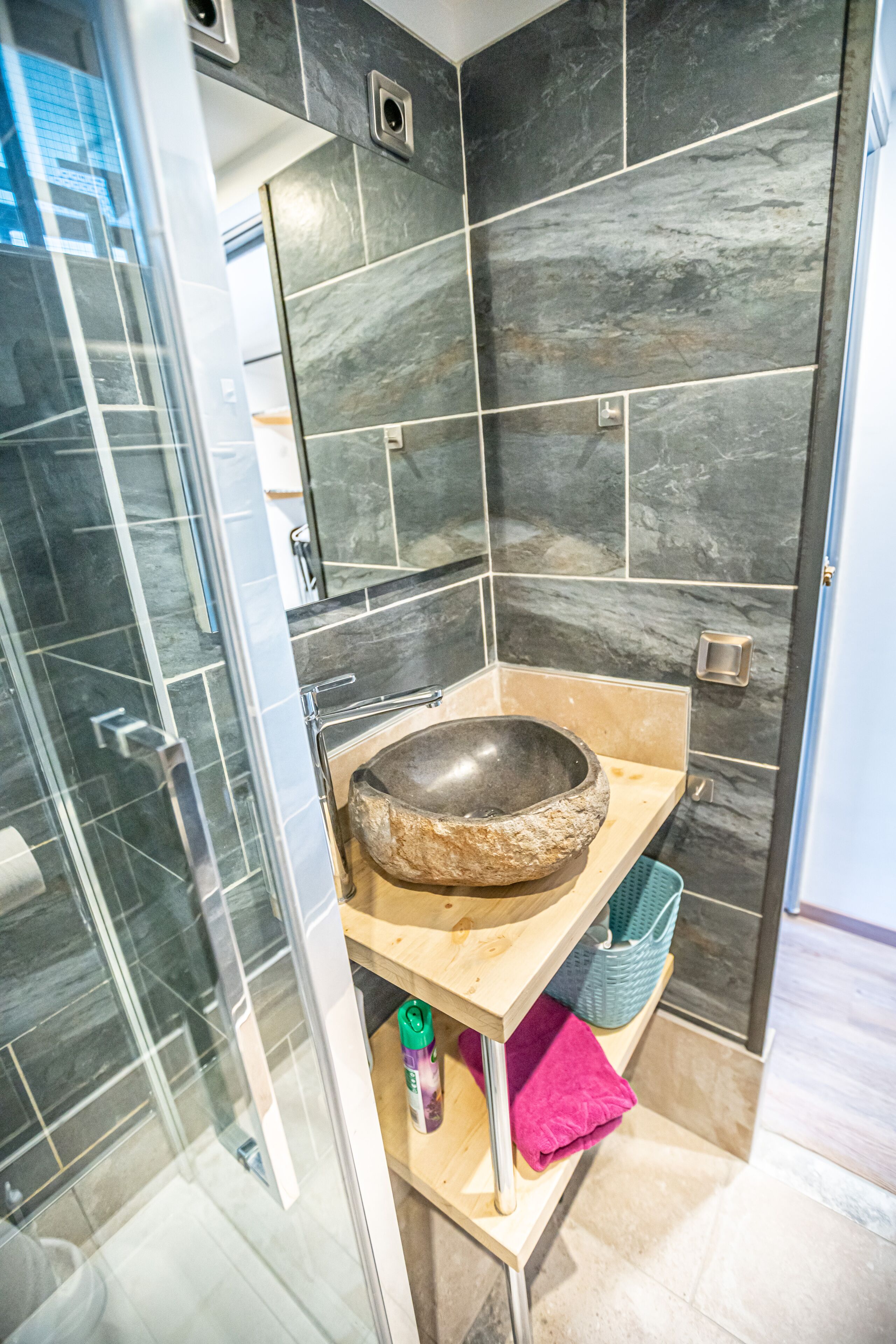 Un baño moderno con lavamanos de piedra, cabina de ducha de vidrio y tocador de madera.