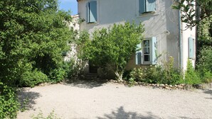 Une maison avec une allée en gravier, un mur en pierre et un jardin agrémenté d’arbres et d’arbustes.