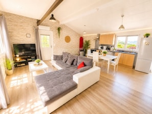 A modern living room with a sectional sofa, a flat-screen TV, a dining area, and a kitchen with a view.