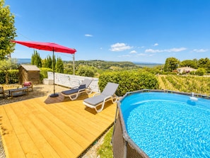 A wooden deck with lounge chairs and a red umbrella, a swimming pool, and a scenic view of hills and vineyards.