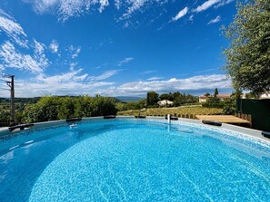 A clear blue swimming pool with a view of a hilly landscape and houses in the background.