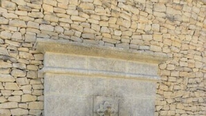 Une fontaine en pierre dotée d’un bassin rectangulaire et d’un élément décoratif central, le tout installé devant un mur en pierre.