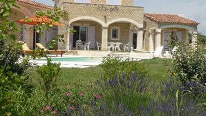 Une villa en pierre dotée d’une piscine, d’un espace extérieur aménagé et d’un jardin où l’on trouve de la lavande et d’autres plantes.