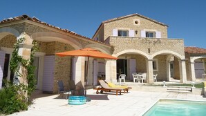 Un bâtiment en pierre doté d’une piscine, d’un espace extérieur aménagé et surplombant un ciel d’un bleu limpide.