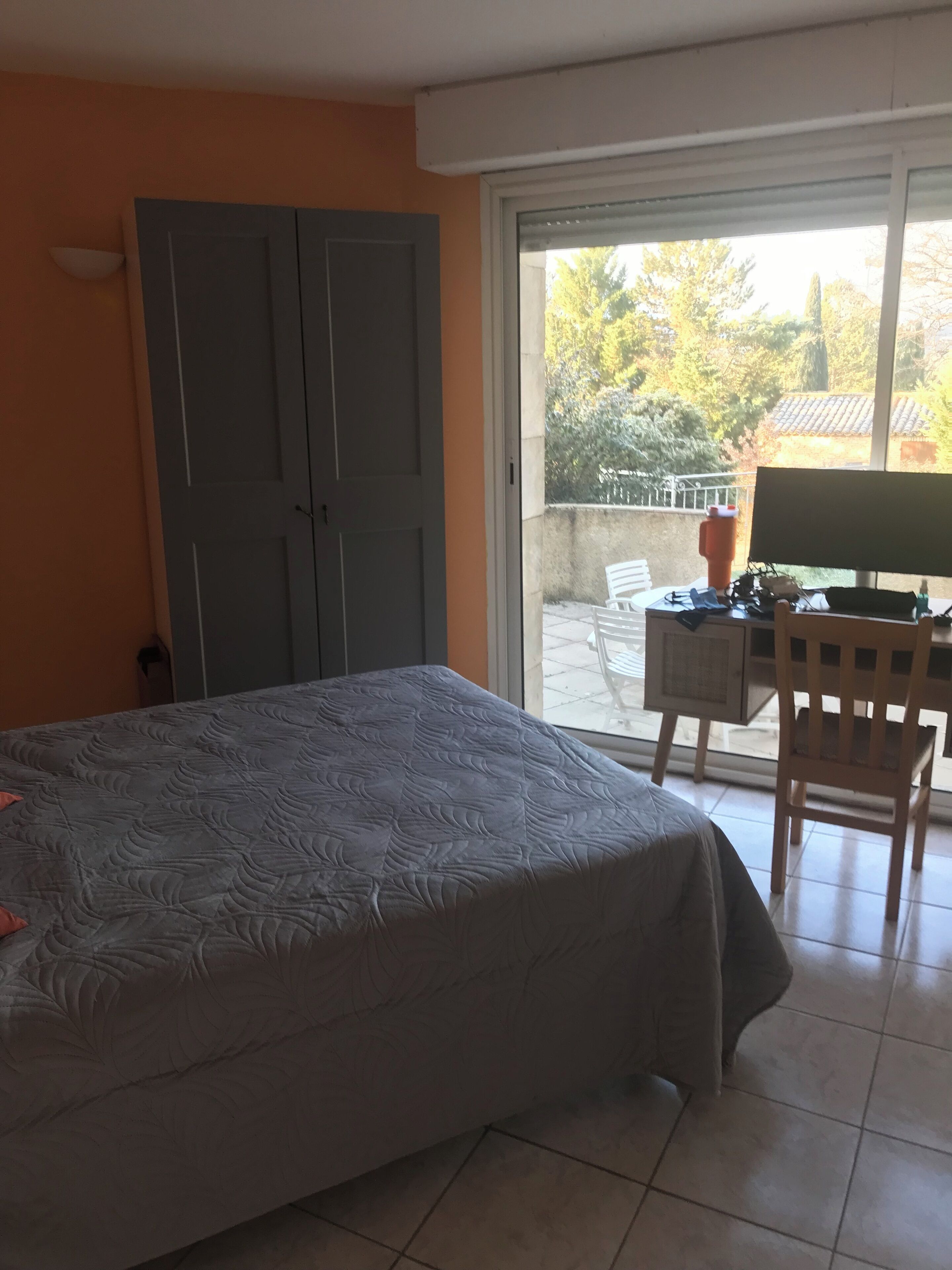 Un dormitorio con cama, escritorio y silla, y un ventanal corredero que da a un espacio exterior.