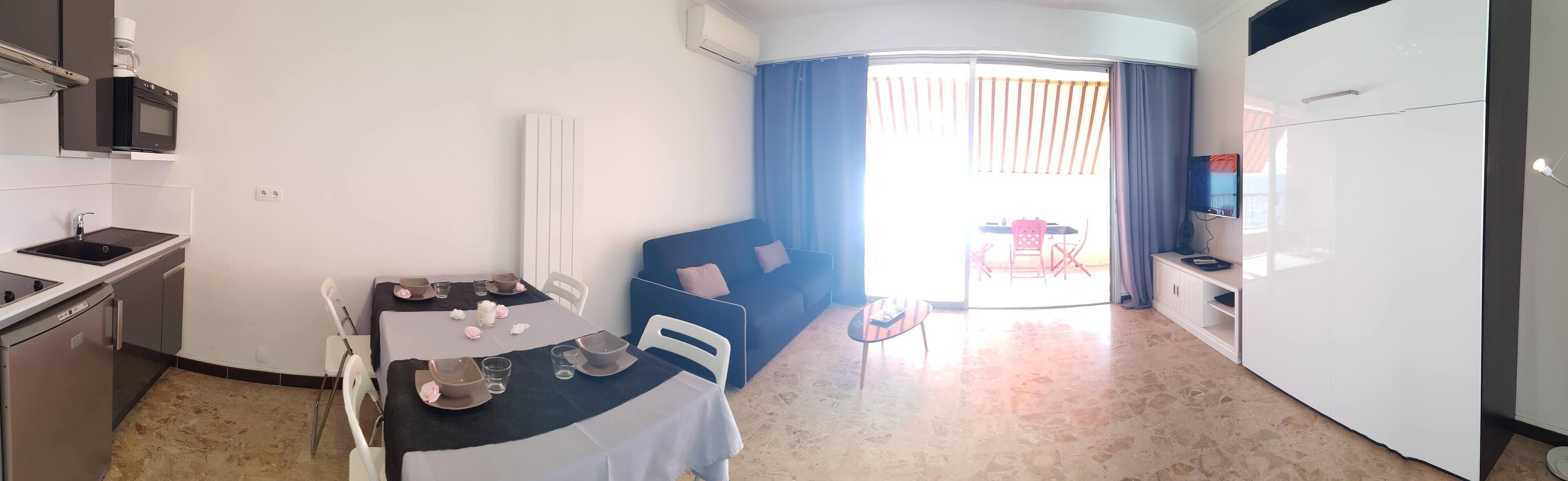A compact room with a kitchenette, a dining area, and a seating area with a sofa and a small table.