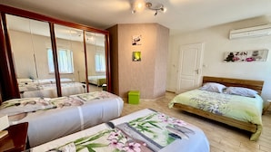 Een slaapkamer met twee bedden, een spiegel, een kledingkast, een deur en een airconditioner.