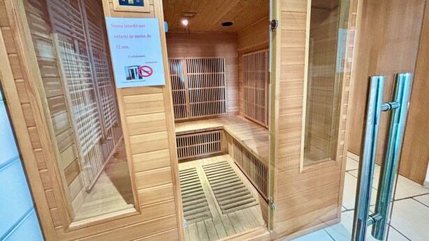 Een sauna met bedieningspaneel, een bord met leeftijdsrestrictie en een houten inrichting.