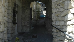 Un arc en pierre mène à une ruelle étroite où une grille métallique est incrustée dans le sol.
