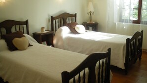 Deux lits simples avec des têtes de lit en bois, une table de chevet avec une lampe et une fenêtre avec des rideaux.