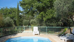 Une piscine entourée d’une clôture verte, avec deux chaises longues et une chaise blanche.