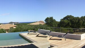 A poolside area with lounge chairs and a view of the sea and hills. - Superb high standing villa Pinarellu (Zonza)