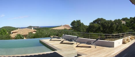 Zona de piscina con sillones de descanso y vistas al mar y las colinas.