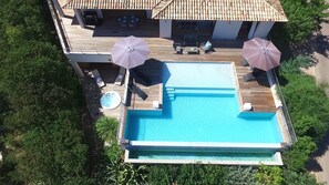 An aerial view of a pool area with a hot tub, lounge chairs, and umbrellas.
