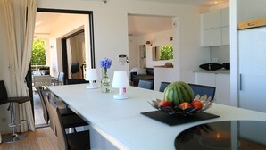 A modern dining area with a long table, two lamps, a vase with flowers, and a fruit bowl. - Superb high standing villa Pinarellu (Zonza)