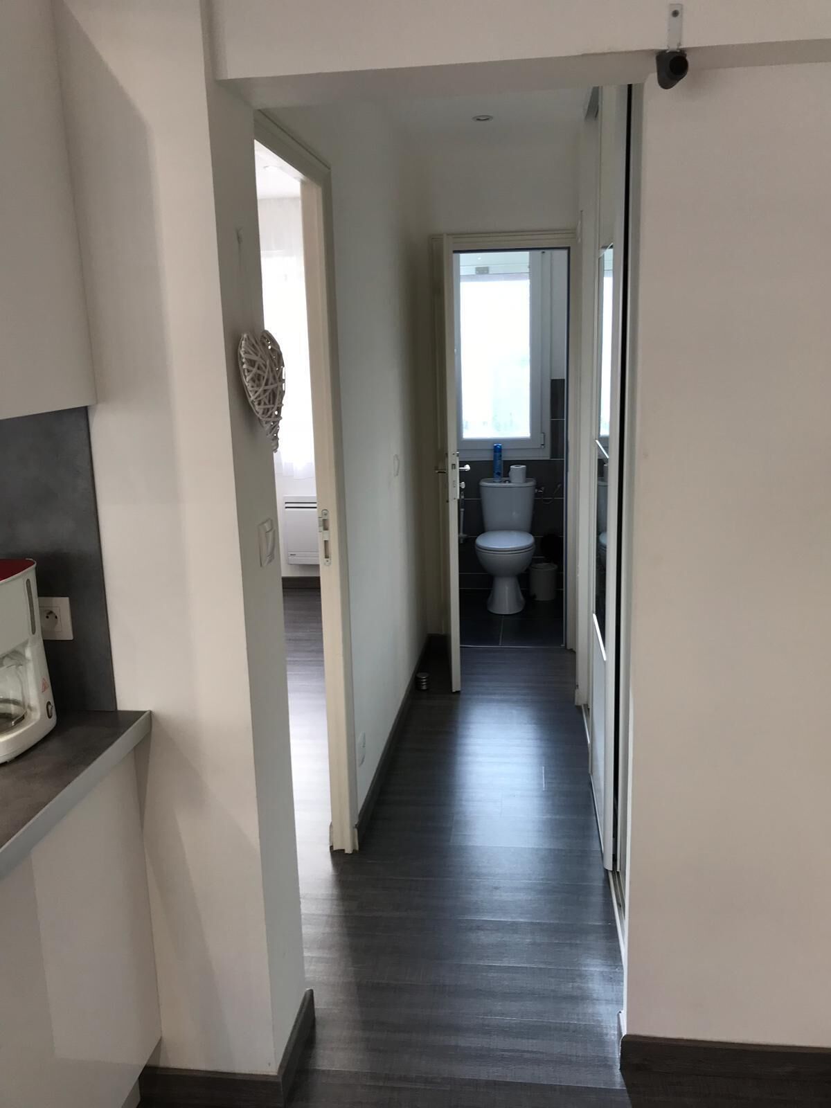 Een smalle gang met een donkere houten vloer, die leidt naar een badkamer met toilet en wastafel.