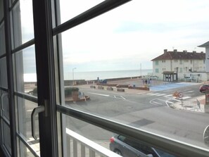 Une vue depuis une fenêtre donnant sur une rue côtière, avec un immeuble, une zone de stationnement et un panneau indiquant la limite de vitesse.