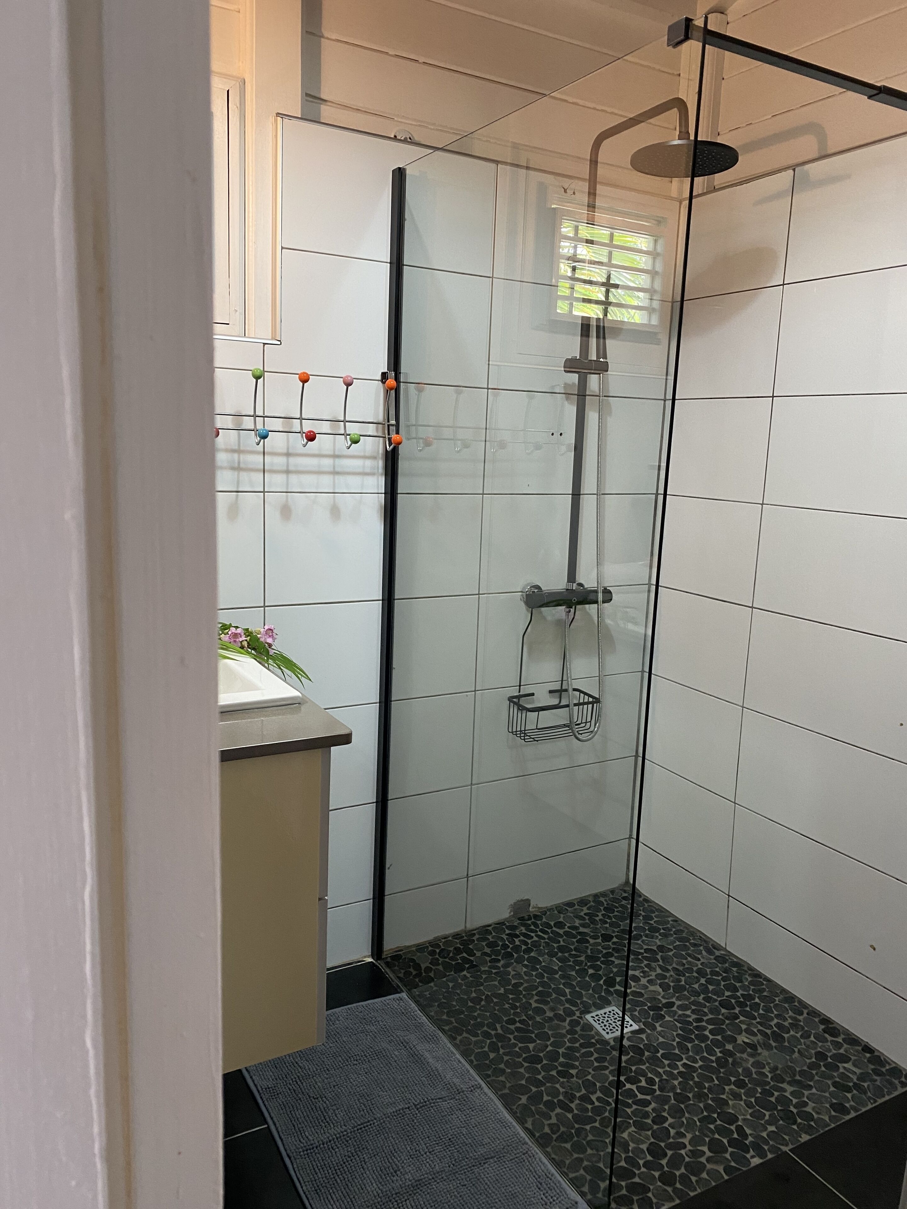 A small, modern bathroom with a glass shower enclosure, a white sink, and a tiled floor.