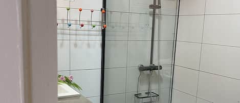 A small, modern bathroom with a glass shower enclosure, a white sink, and a tiled floor.