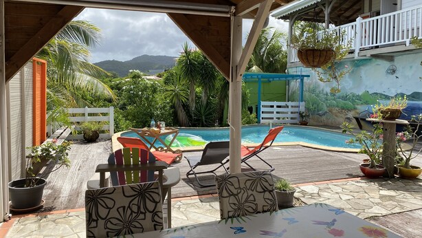 A covered outdoor area with a pool, lounge chairs, and potted plants. - T4 design in lush greenery, sea view and swimming pool, 10 minutes from the beaches.  (LES TROIS ILETS)