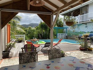 A covered outdoor area with a pool, lounge chairs, and potted plants.