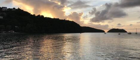 A calm body of water reflecting the sky with boats and a distant island.