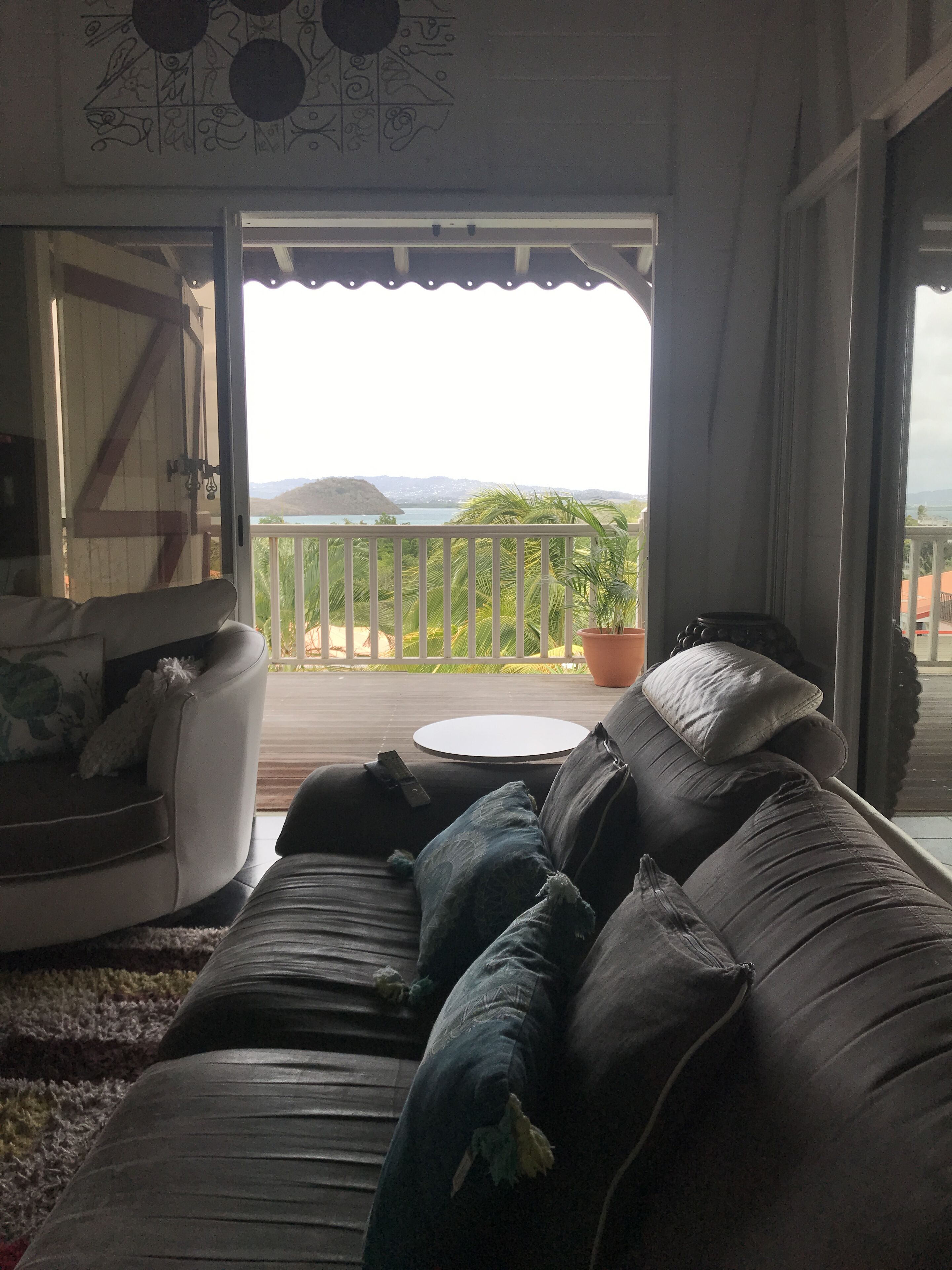 A cozy living area with a sofa and a small table, a balcony with a railing, and a view of the landscape.