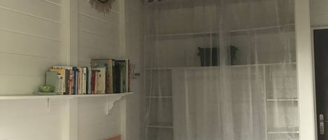 Une pièce comprenant un lit, une étagère remplie de livres, un élément décoratif fixé au mur et une fenêtre ornée d’un rideau léger.
