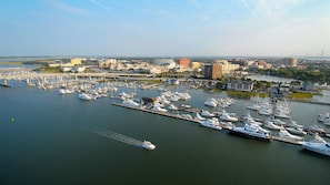 Uma marina com vários barcos atracados, uma ponte ao fundo e um horizonte urbano com edifícios e um rio.
