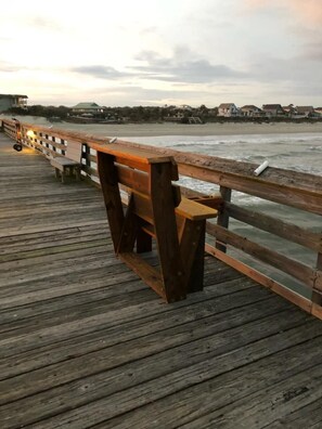 A wooden pier with benches, overlooking a beach and ocean.