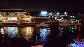 Uma marina à noite com barcos atracados, um restaurante à beira-mar e um edifício com letreiros iluminados.