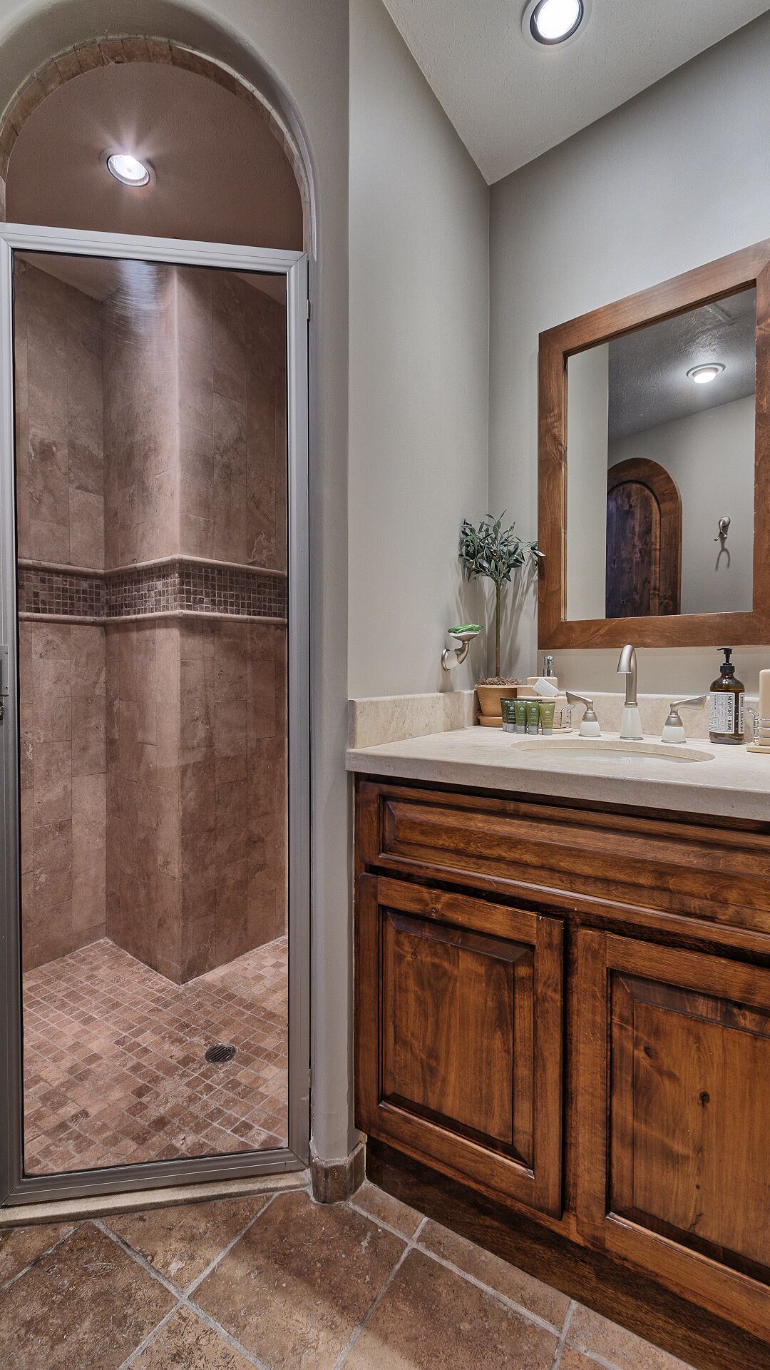 Une salle de bain avec une douche à l’italienne, un meuble-lavabo avec un miroir et un sol carrelé.