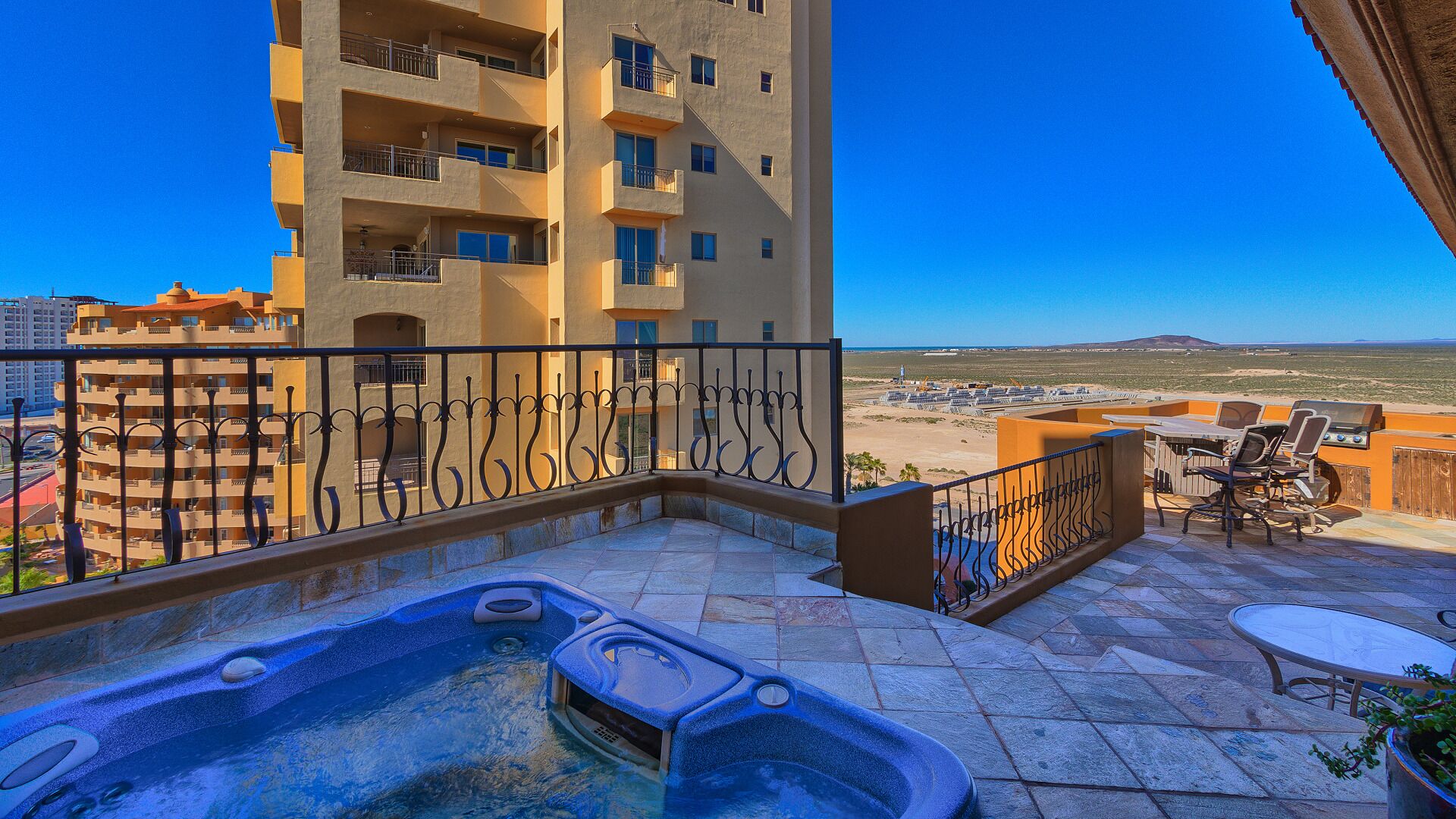 A rooftop terrace with a hot tub, outdoor seating, and a view of a desert landscape.