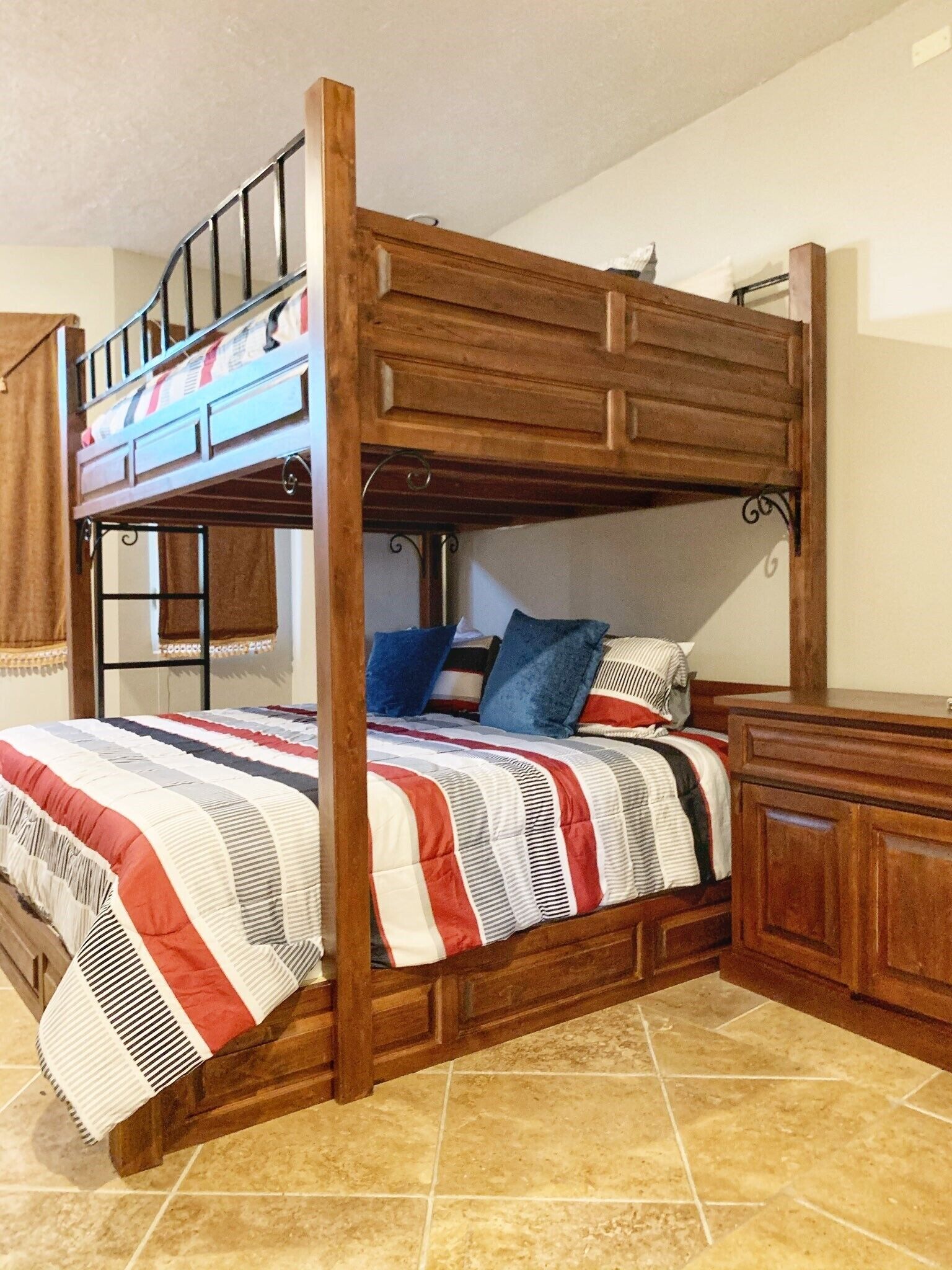Una cama litera con estructura de madera, una colcha a rayas y una mesita de noche con cajón.