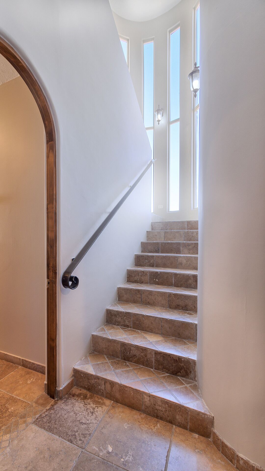 A staircase with a handrail, leading to a landing with windows.