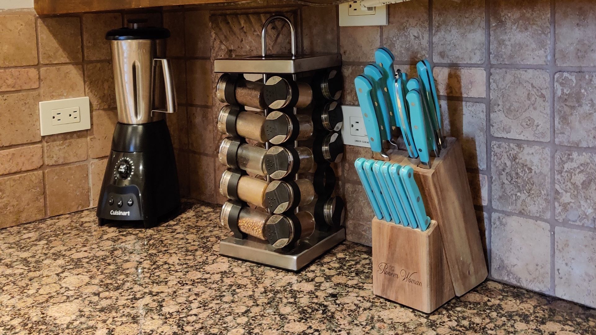 A kitchen with a granite countertop, a black coffee maker, a spice rack, and a knife block.
